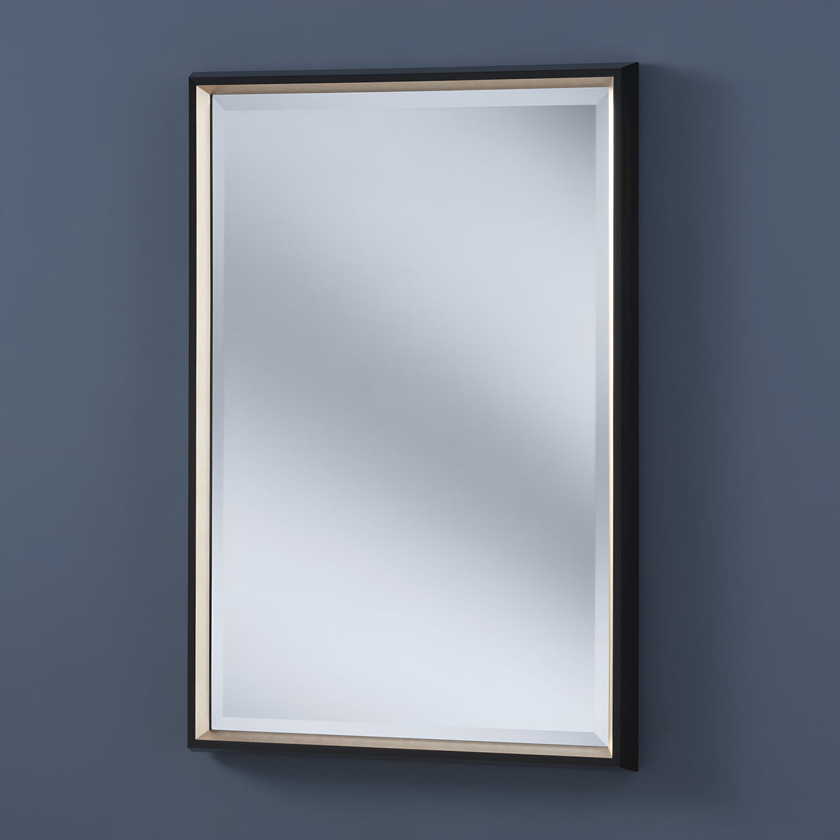 The Lirion Rectangle Wall Mirror - Black & Gold, elegantly placed against a grayish-blue wall, features a stylish frame and slightly beveled edge that enhance its contemporary design by softly reflecting light throughout the room.