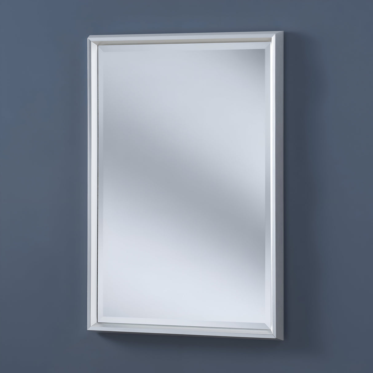 The Lirion Rectangle Wall Mirror - Silver hangs on a dark gray wall, its clear reflective surface adding elegance to your decor. Subtle reflections dance across its sleek, modern design.