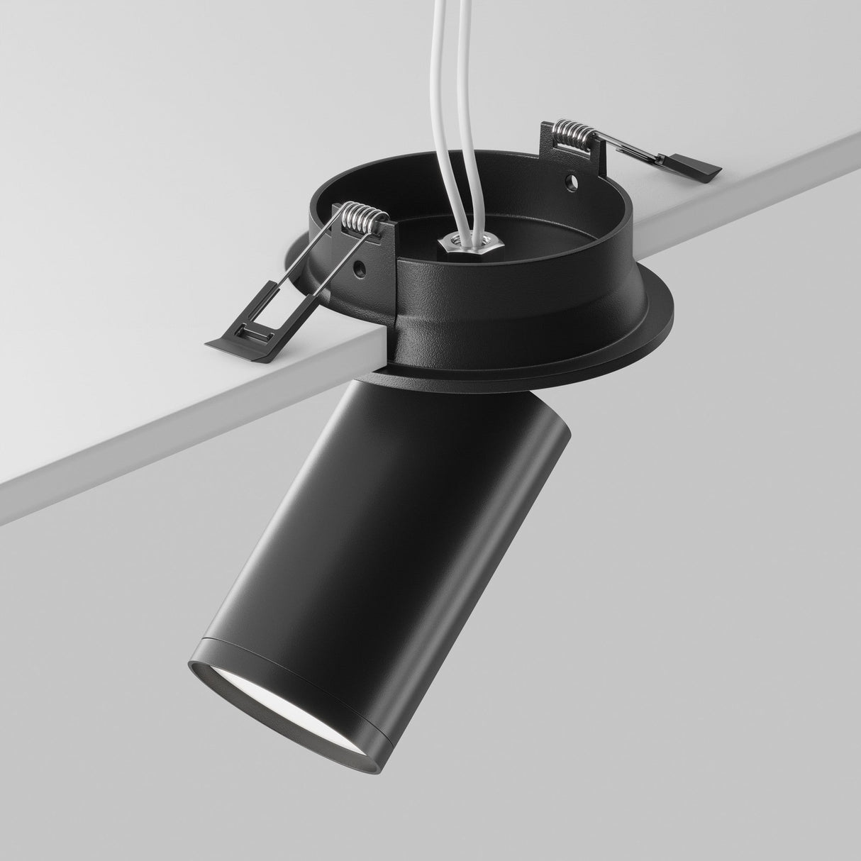 The Focus S Single Recessed Spotlight in black, with a cylindrical form, adorns minimalist white ceilings. Angled downward, its exposed wiring offers contrast while mounting clips ensure secure installation.
