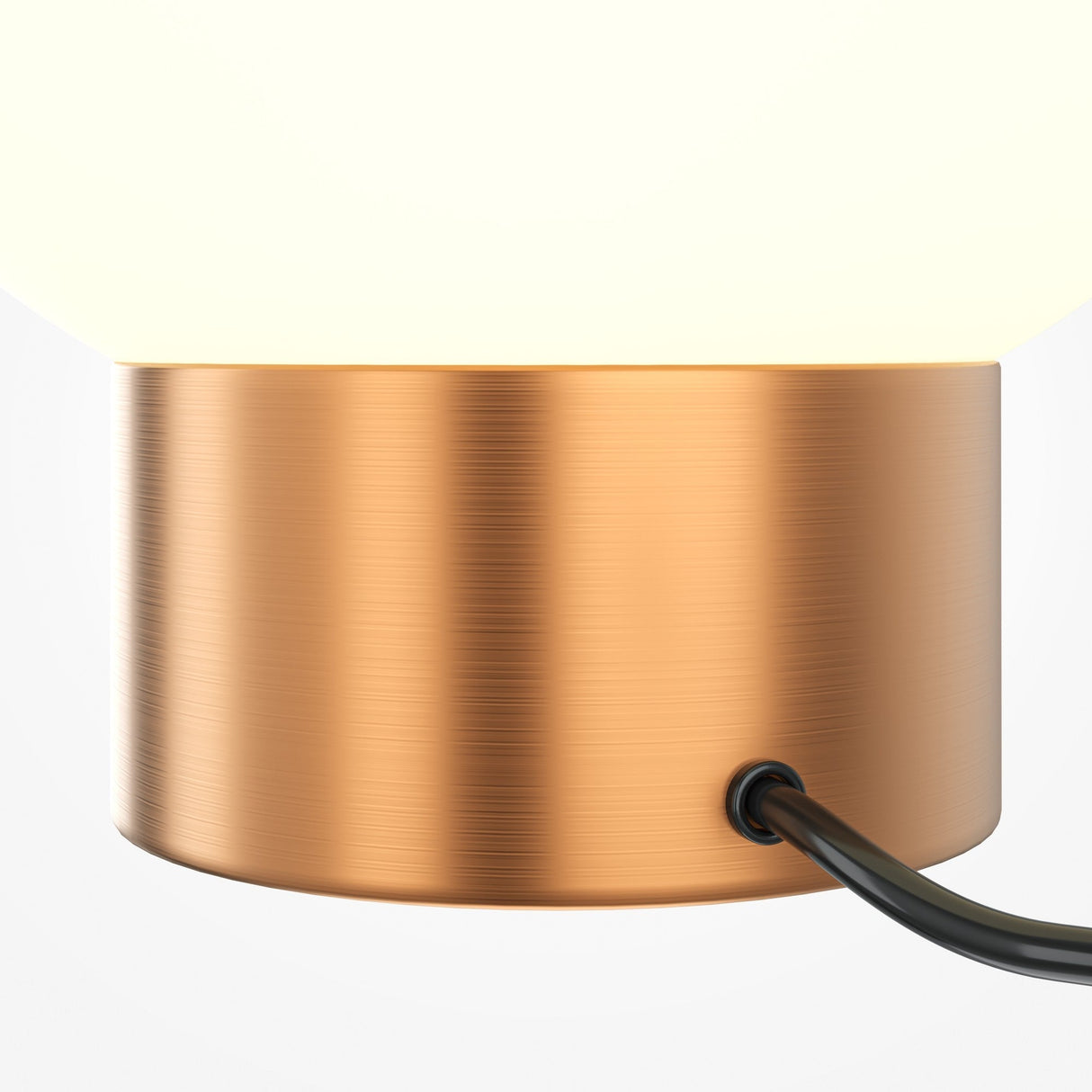 The Basic Form Table Lamp features a cylindrical gold base and frosted white glass top. A black cord plugs into the side, while its warm glow contrasts against a plain white background.