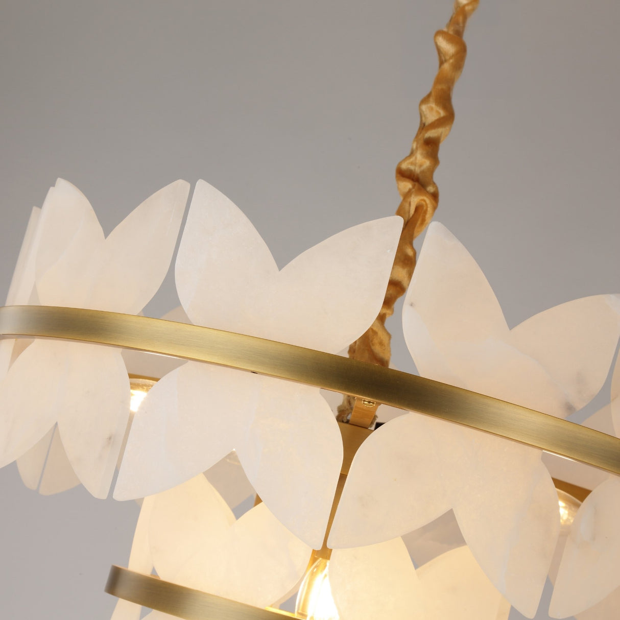 Close-up of Niori Petraia 2 Tier Floral Alabaster Chandelier with white petals on brushed brass rings and gold fabric-wrapped cable.