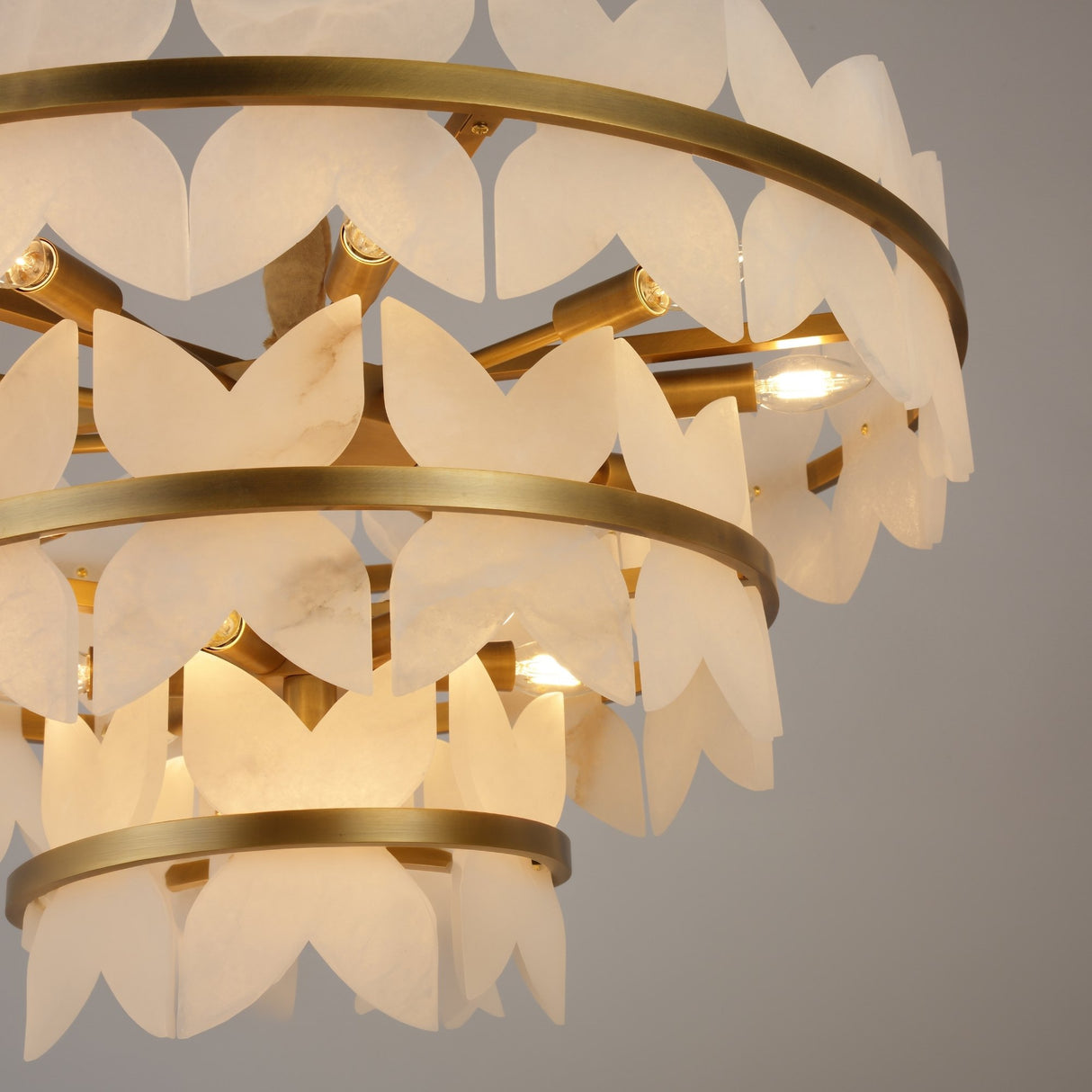 Close-up of Niori Petraia 3 Tier Floral Alabaster Chandelier showing scalloped white alabaster petals on brushed brass rings with lit E14 candle bulbs.