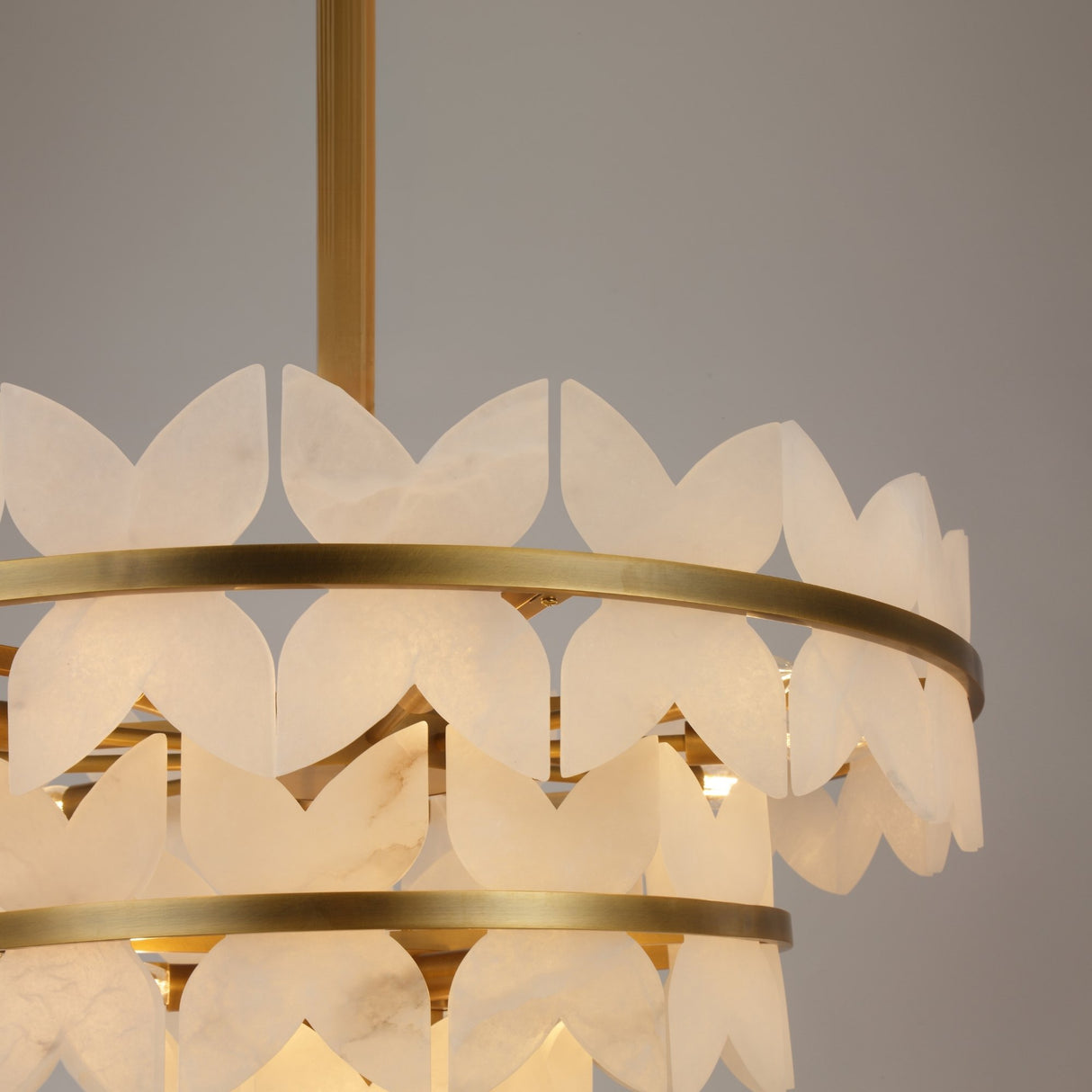 Close-up of Niori Petraia chandelier showing tiered brushed brass rings edged with scalloped white alabaster petals on a suspension rod.