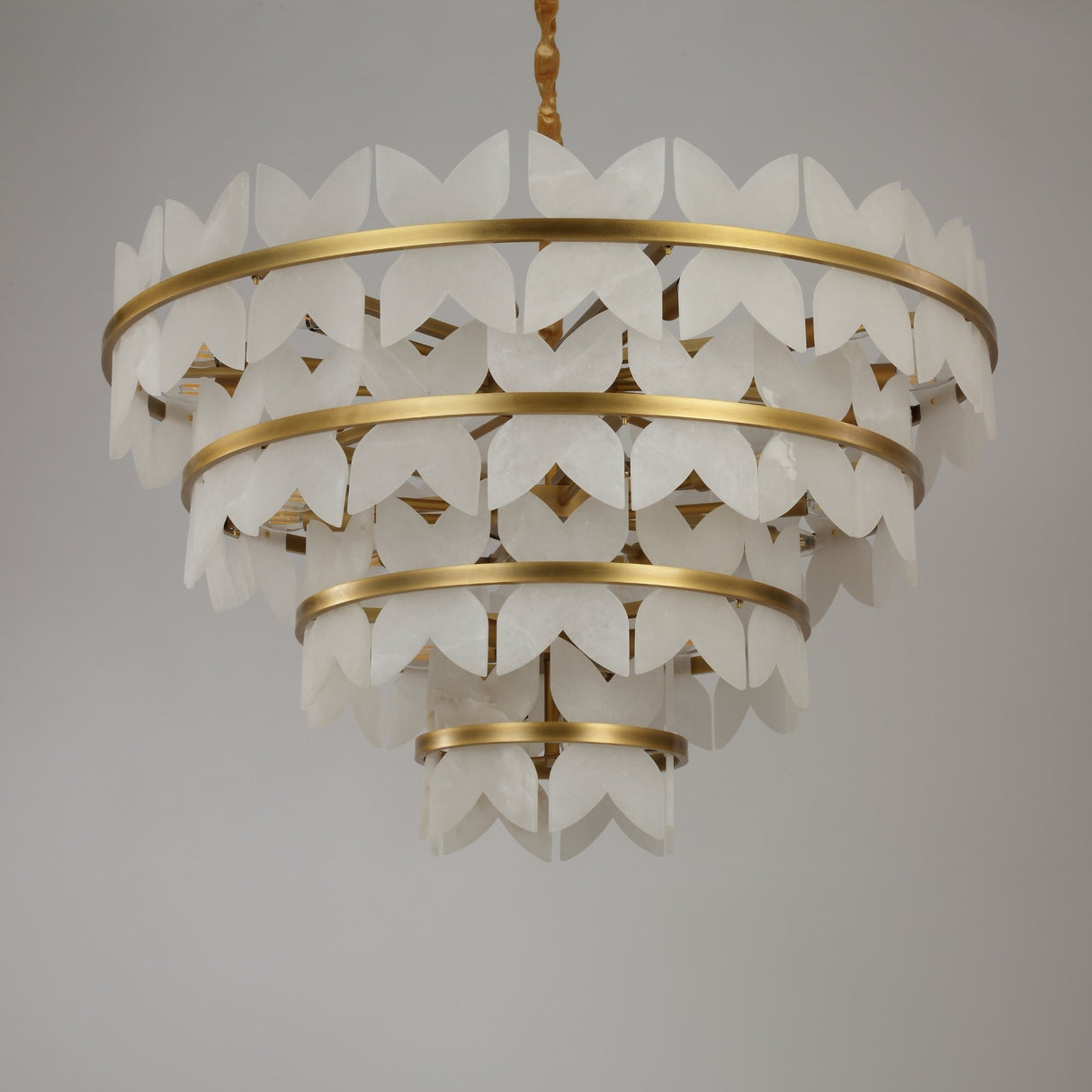 Niori Petraia four-tier chandelier with alabaster floral petals on brushed brass rings, suspended from a rope-wrapped drop against a light background.