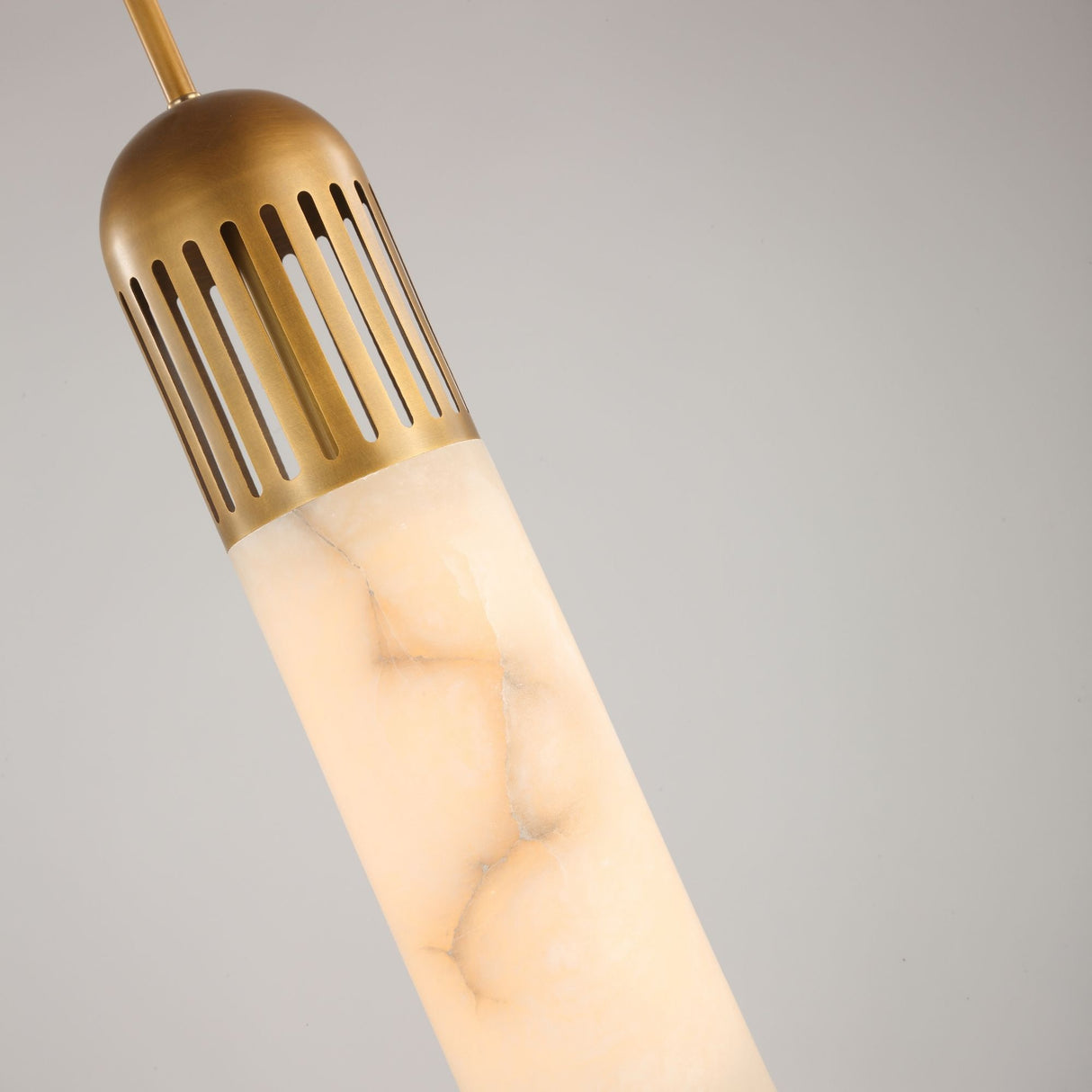Zerith LED Alabaster Tube Pendant Light in Brushed Brass, close-up of the fluted brass collar and marbled alabaster cylinder against a plain grey background.