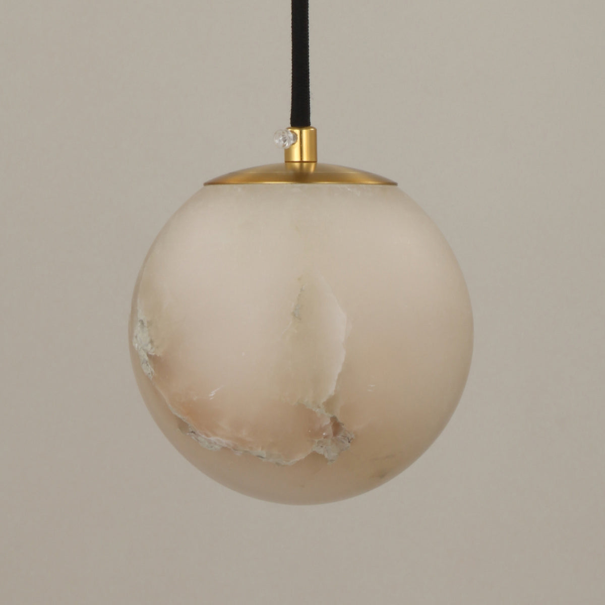 Lyvane extra small alabaster globe pendant light with brushed brass cap and black fabric cable, natural stone veining, on a plain light background.