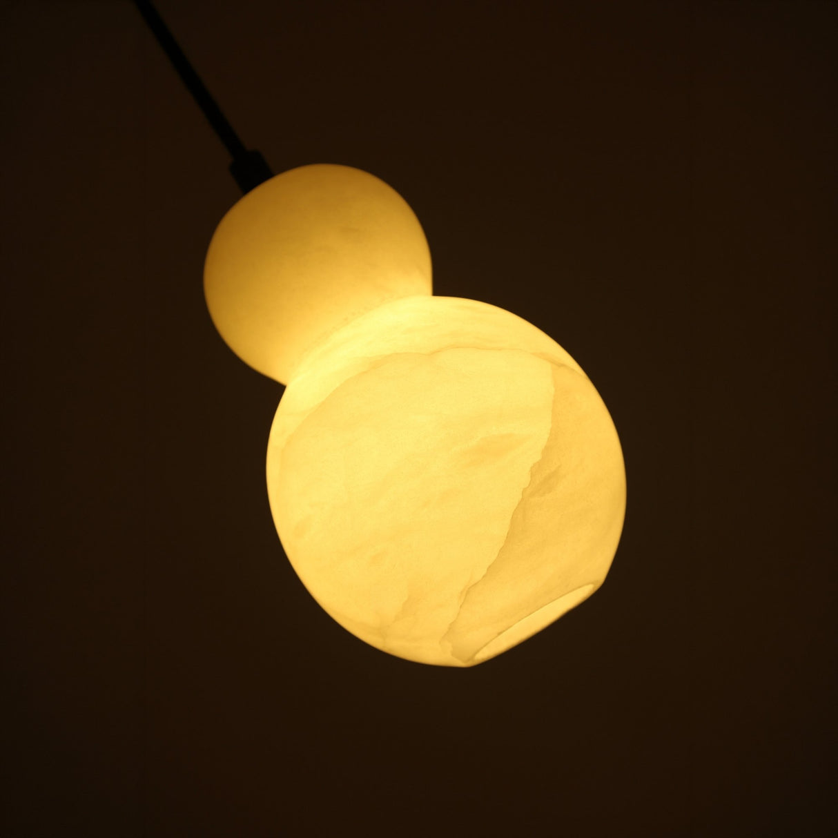 Niori Orlune LED pear pendant light glowing warm white, showcasing the alabaster double-gourd shade with natural veining against a dark background.
