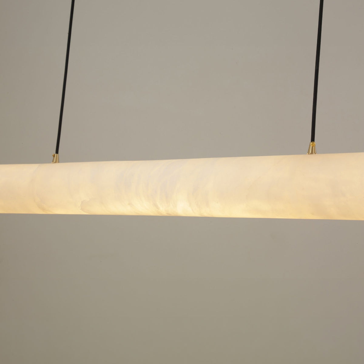 Zareon LED Large Linear Alabaster Chandelier in soft white, close-up of the cylindrical stone diffuser glowing warm white, suspended on twin black cables against a plain grey background.