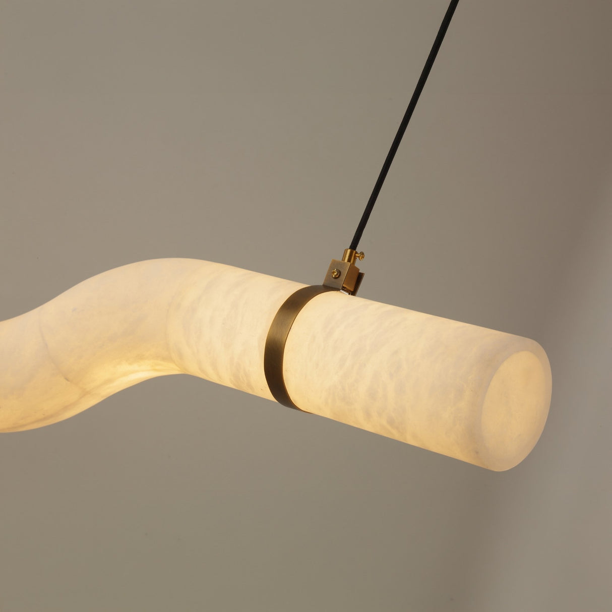 Niori Zareon LED small curved alabaster chandelier in soft white with brushed brass strap and canopy, illuminated against a neutral background.