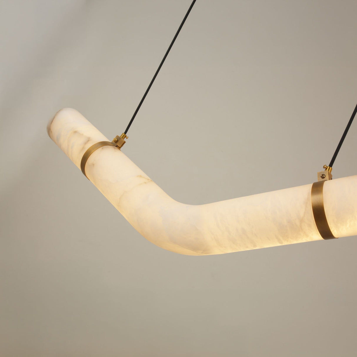 Zareon Small LED Chevron Alabaster Chandelier with angled boomerang profile, brushed brass cuffs at the bend, and twin black suspension cables against a plain grey background.