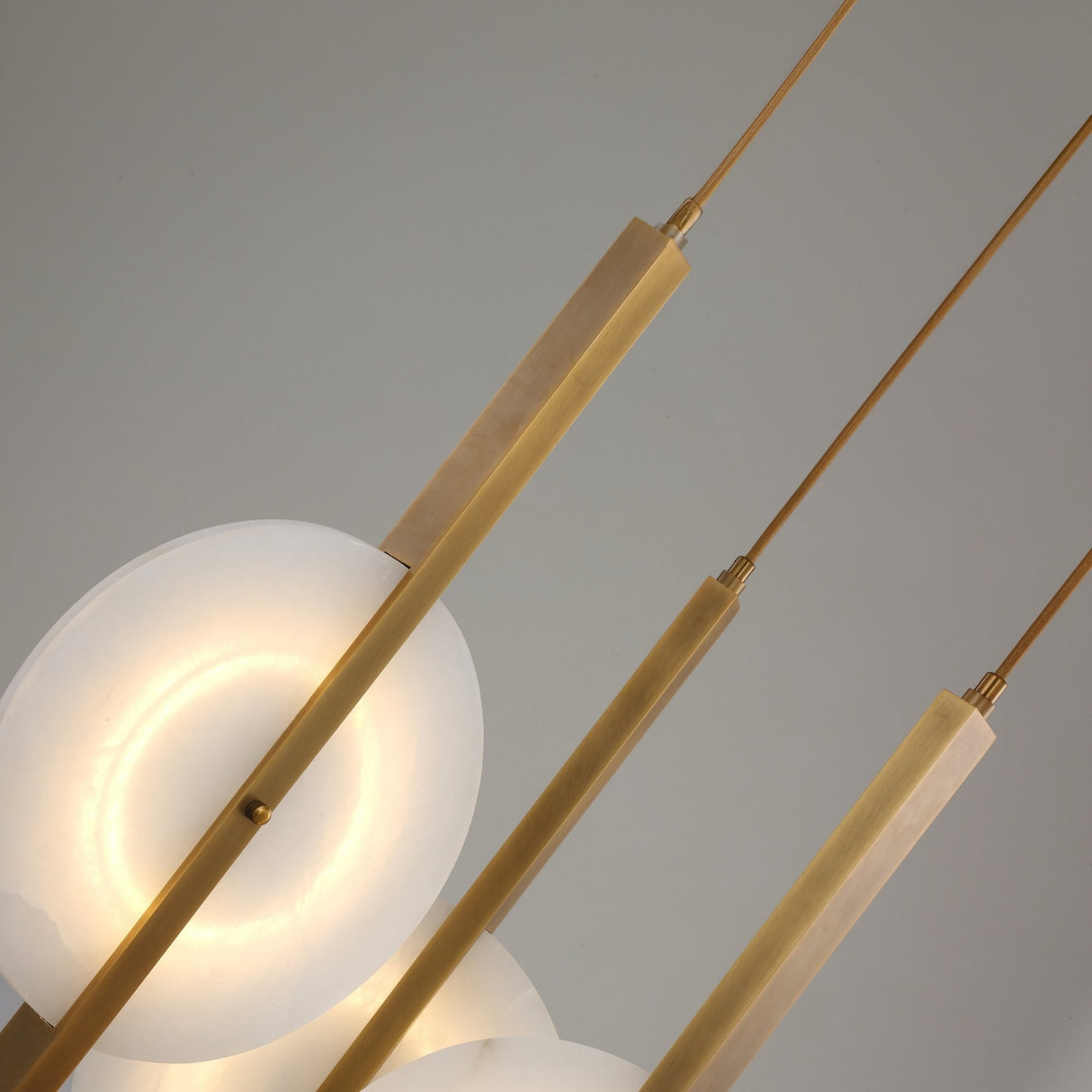 Close-up of Niori Elyra 3 Light LED Alabaster Cluster Chandelier with brushed brass blade stems, suspension cables, and a warm-lit translucent alabaster disc.