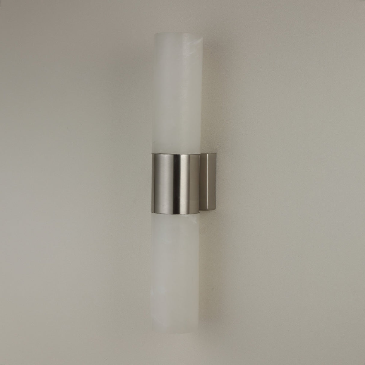 Niori Fiora LED alabaster wall light with two vertical cylindrical columns joined by a satin nickel band, mounted on a plain light wall.
