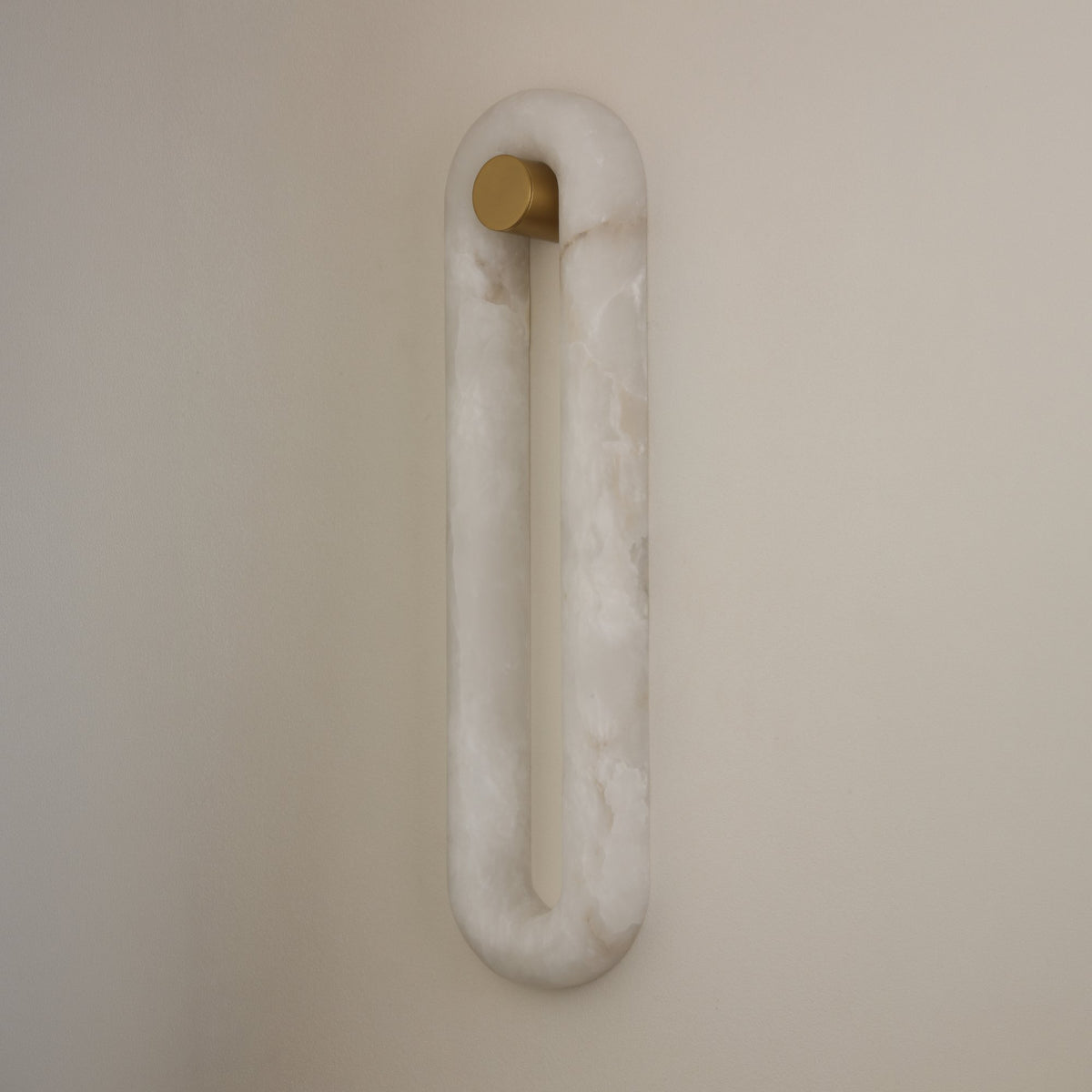 Serava LED Alabaster Wall Light Large in soft white, an elongated oval loop with brushed brass mounting bracket, mounted on a plain neutral wall.