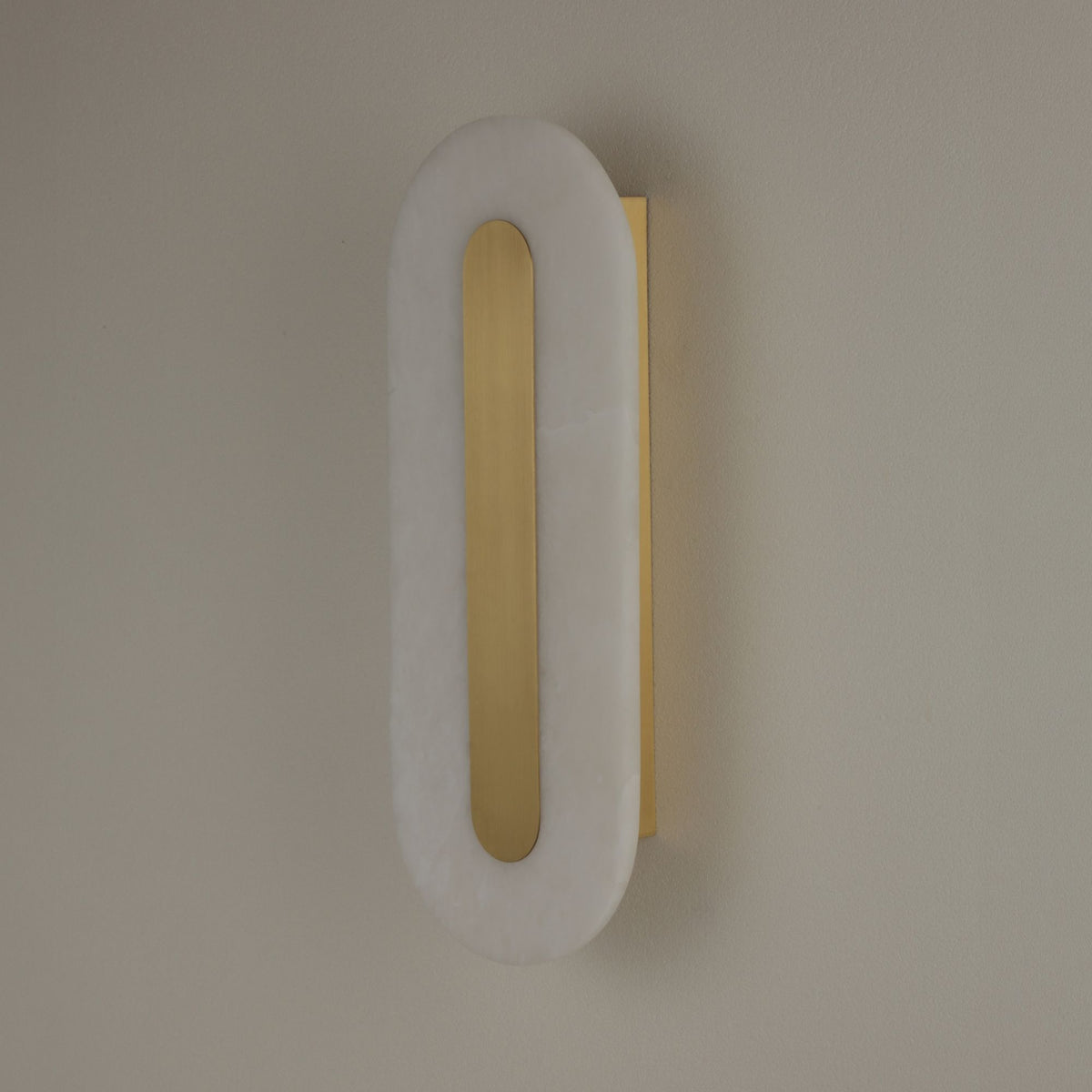 Niori Averra large oval alabaster wall light with brushed brass spine and backplate, mounted on a neutral wall.