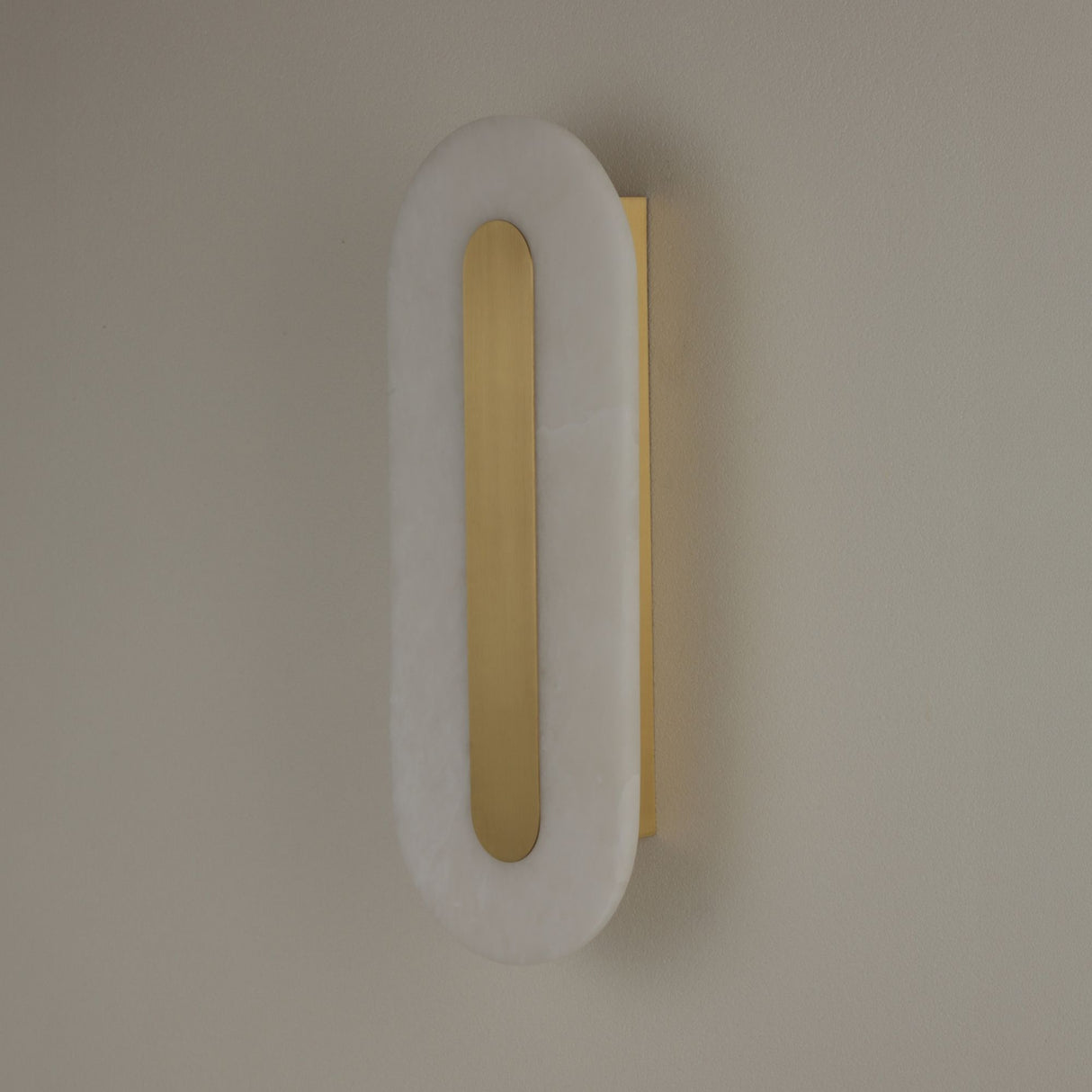 Niori Averra 800mm alabaster wall light with elongated rounded white panel and recessed brass linear detail, mounted on a neutral wall.
