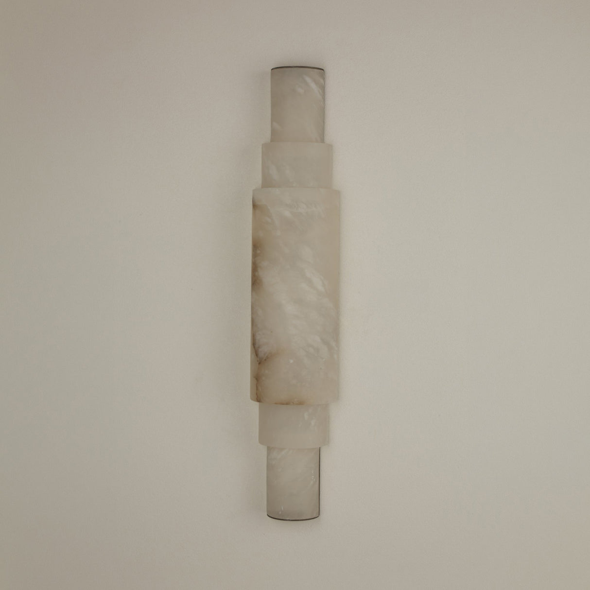 Niori Aurelia LED wall light in stacked natural Spanish alabaster cylinders with brushed brass end caps, mounted vertically on a plain neutral wall.