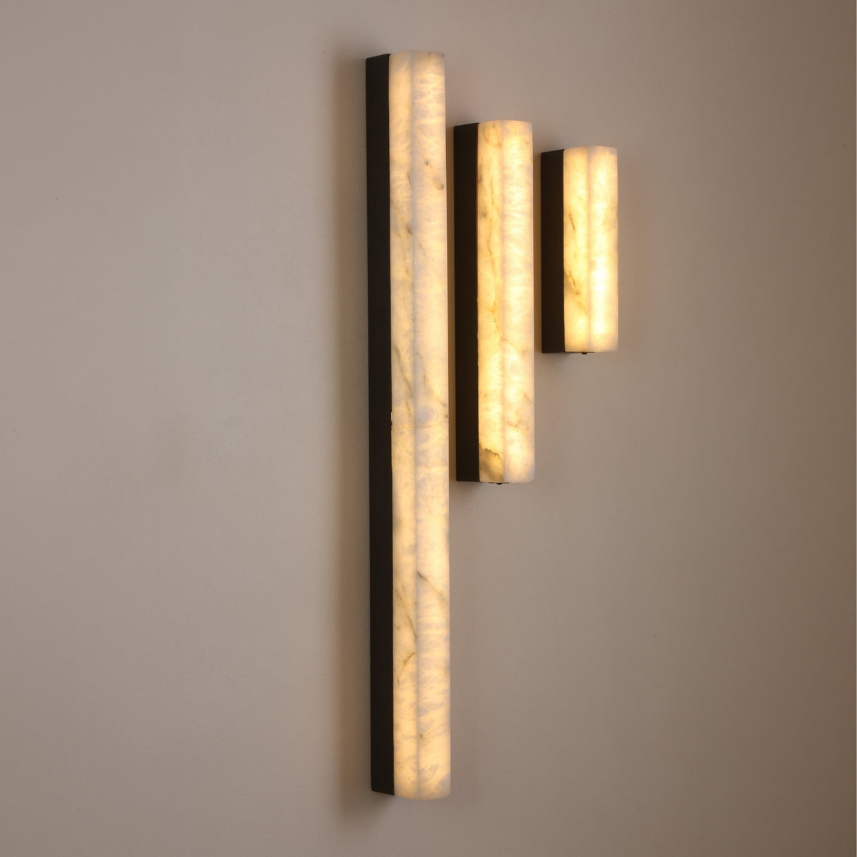 Niori Cornova 450mm slim linear alabaster wall lights in matte black, shown in three staggered heights glowing warm white against a neutral wall.