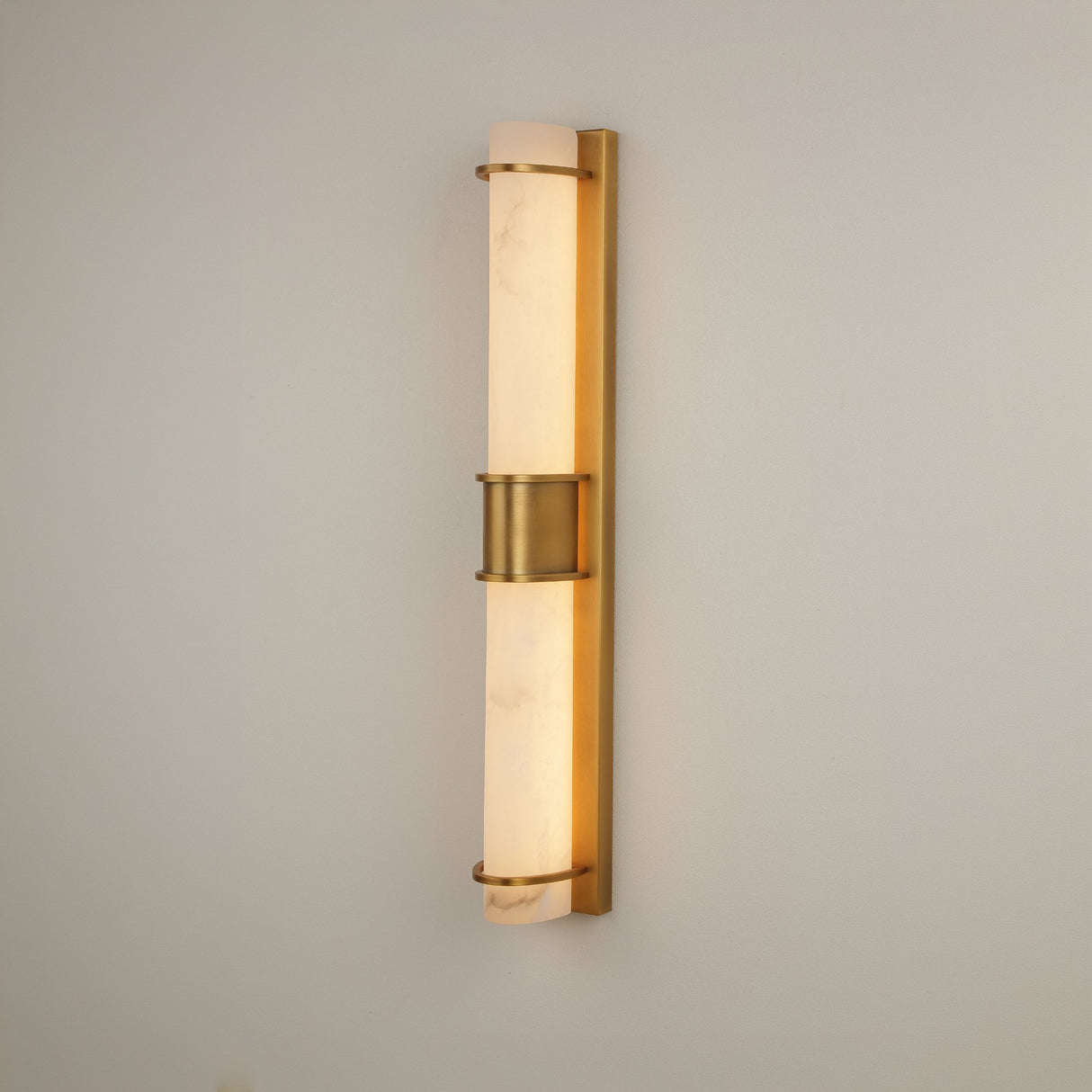 Niori Averna LED framed alabaster wall light with two stacked cylinders in a brushed brass frame and central collar, mounted on a light wall.