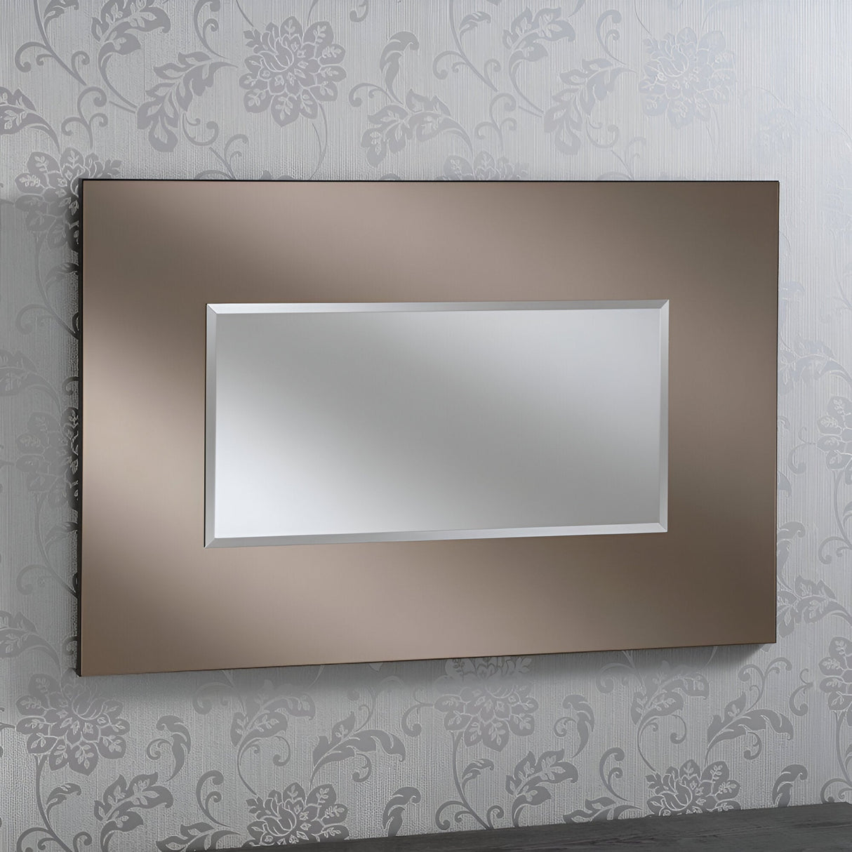 A Clarius Rectangle Wall Mirror in Bronze, measuring 92x61cm, hangs on a wallpapered wall adorned with light gray floral designs on a slightly darker gray background. The mirror's metallic decor provides a striking contrast to the floral-patterned wallpaper.