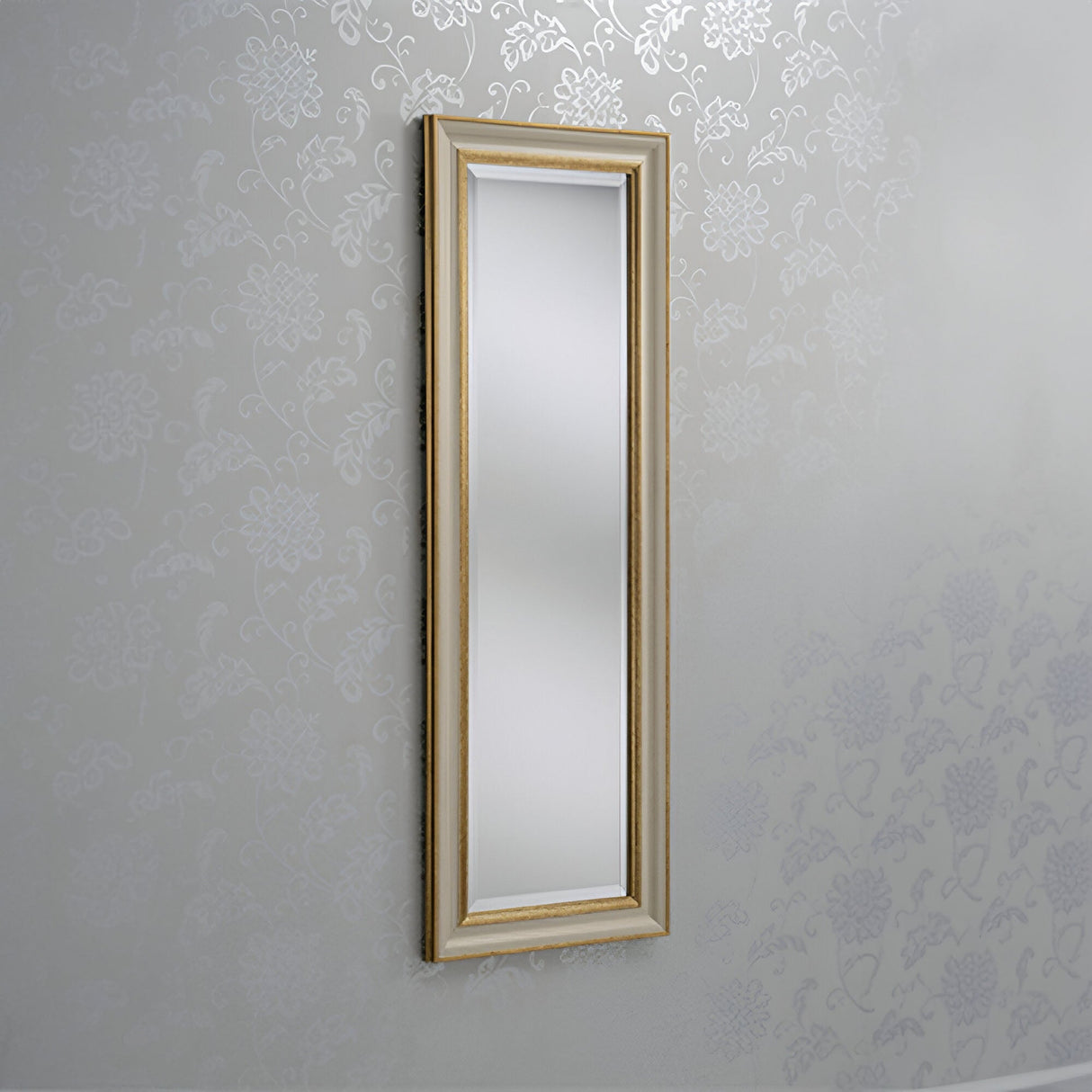 The Napoli Rectangle Wall Mirror in gold and ivory is mounted on a patterned wall. The subtle floral designs in light gray offer an elegant decor backdrop, exuding the charm of luxurious home decor.