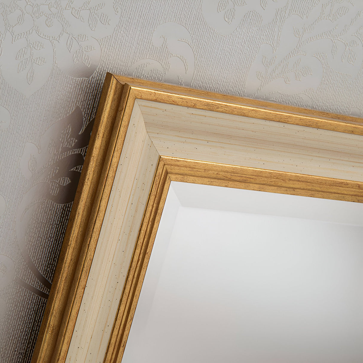 A close-up of the Napoli Rectangle Wall Mirror in gold and ivory, showcasing its luxurious frame design. The background features textured wallpaper with a subtle floral pattern, enhancing the elegant ambiance.