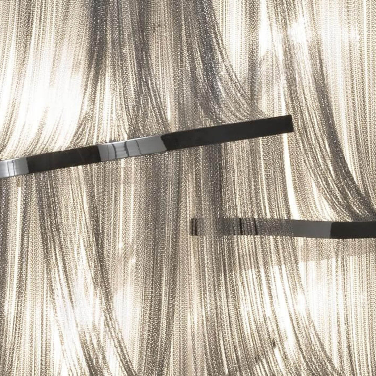 A close-up of the Mireya 4 Light Metal Chain Veil Wall Light in Nickel, featuring draped metallic chains and black bars, illuminated to create a shimmering, textured abstract pattern.