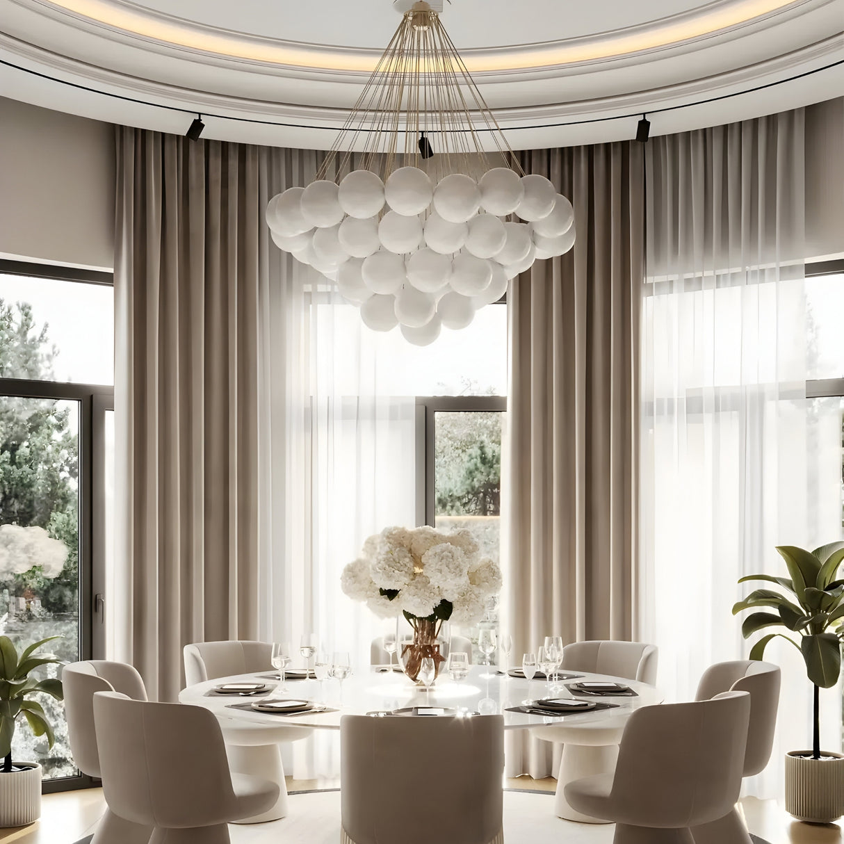 Elegant dining room with a round white table, six chairs, and a vase of white flowers. Large windows with sheer curtains and nearby green plants. The Orb 37 Light Cluster Suspension - Black hangs above with frosted glass orbs.