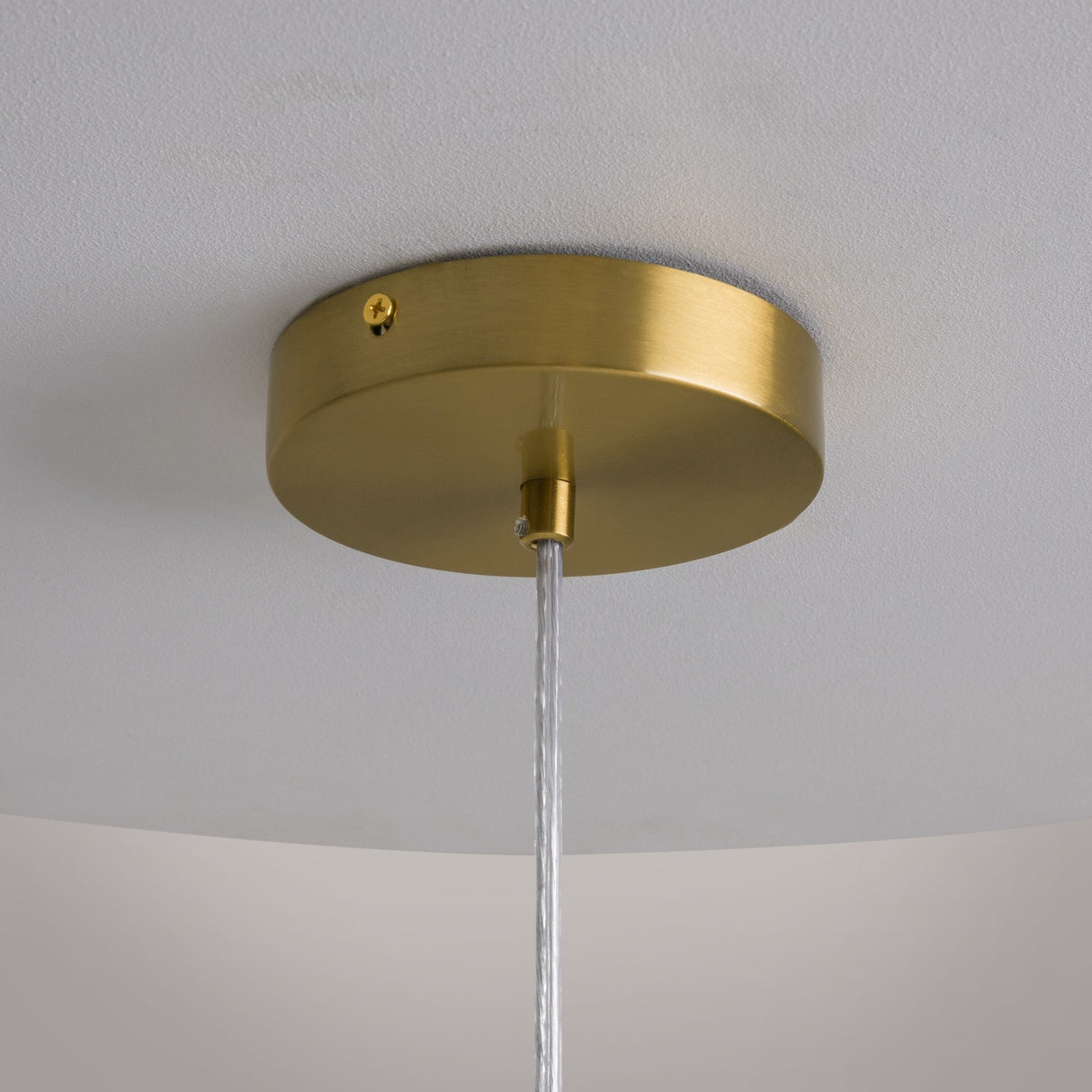 Close-up of the Cometa LED Pendant Light in brushed gold with a clear glass finish. A translucent cord extends from its center, set against a plain white ceiling.