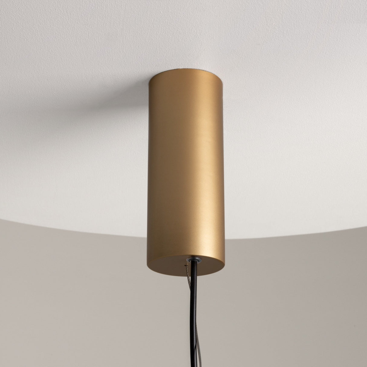 The Enigma Adjustable LED Pendant Light in brass and black hangs from the white ceiling, featuring black wires trailing down for a minimalist aesthetic.