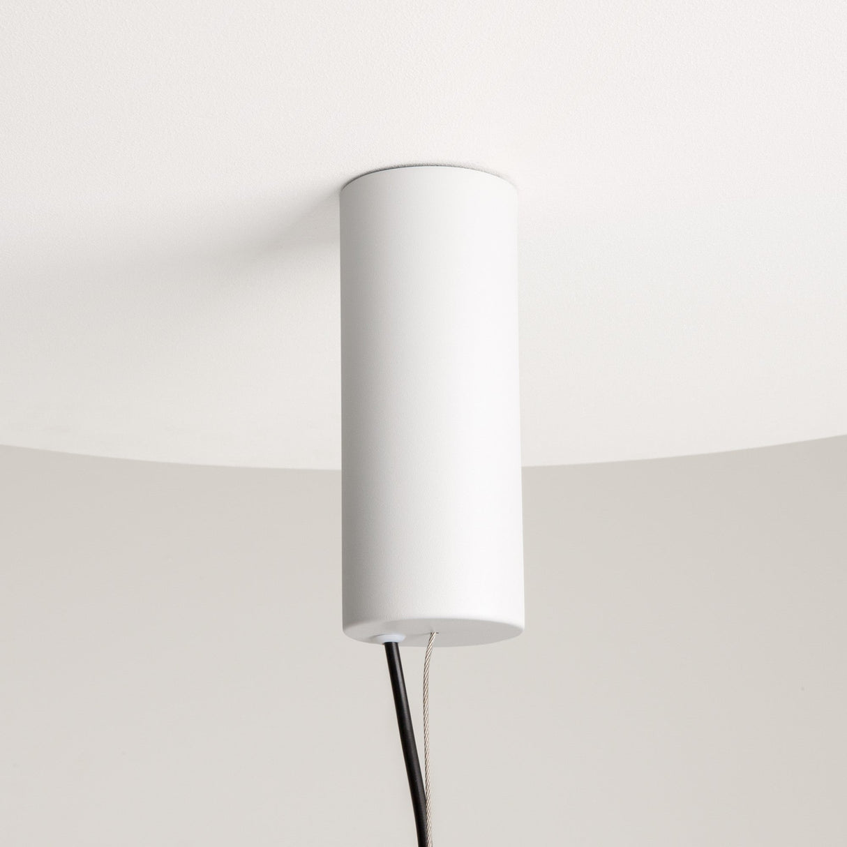 The Enigma Adjustable LED Pendant Light in white with black features a sleek, cylindrical design elegantly attached to the ceiling. Two black cords hang below against a white background, allowing adjustable lighting to suit any ambiance.