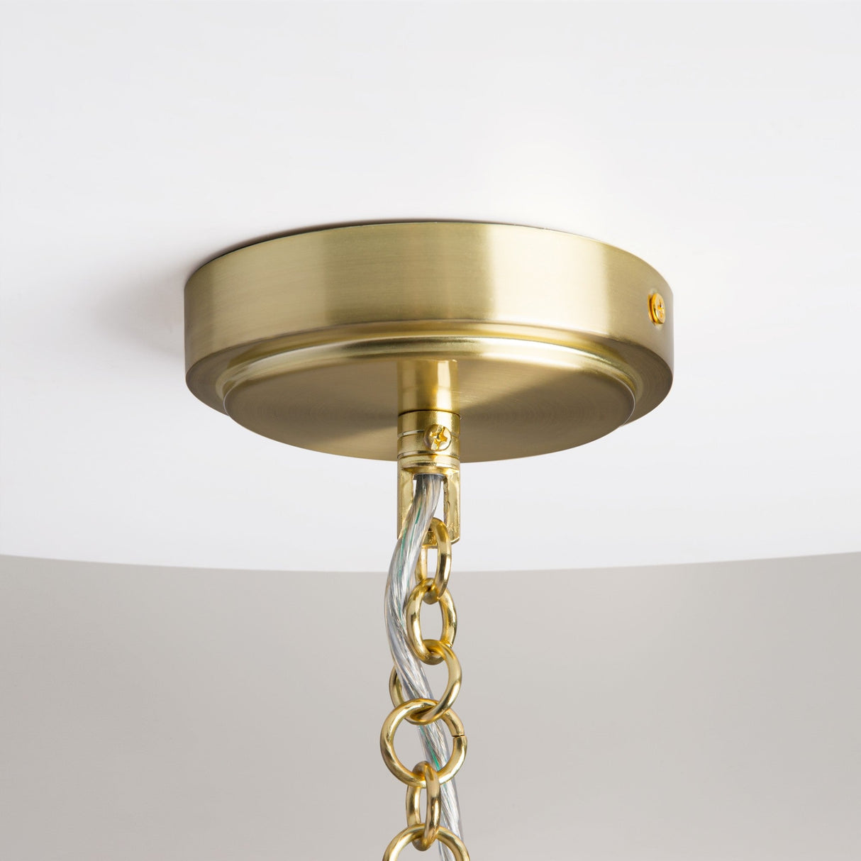 Close-up of the Impressive 5 Light Chandelier - Golds brass ceiling mount adorned with modern elegance, featuring gold-tone chains and a transparent cord gracefully descending against the pristine white ceiling.