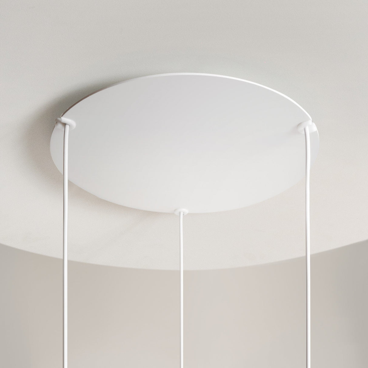 The Reflex 3 Light LED Disc Pendant in white, featuring a round design with three cables, provides ambient illumination and complements the modern, minimalist decor by seamlessly blending into the smooth, light-colored ceiling.