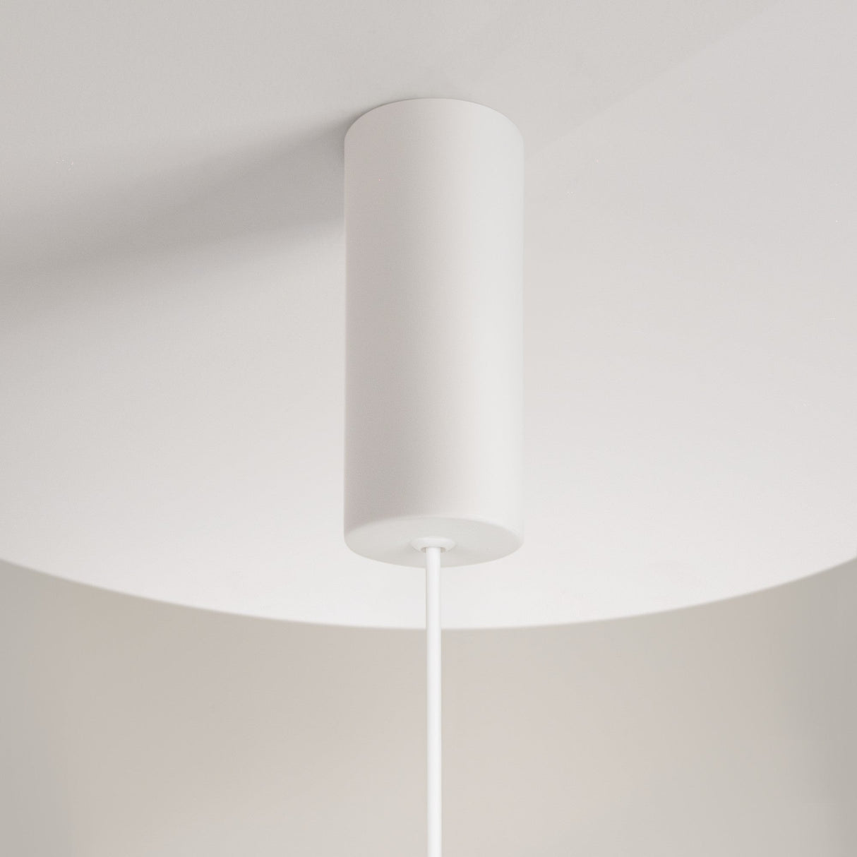 The Reflex 1 Light LED Disc Pendant - White features a minimalist design with a cylindrical white shade and adjustable downward-hanging wire, complementing off-white ceilings and walls.