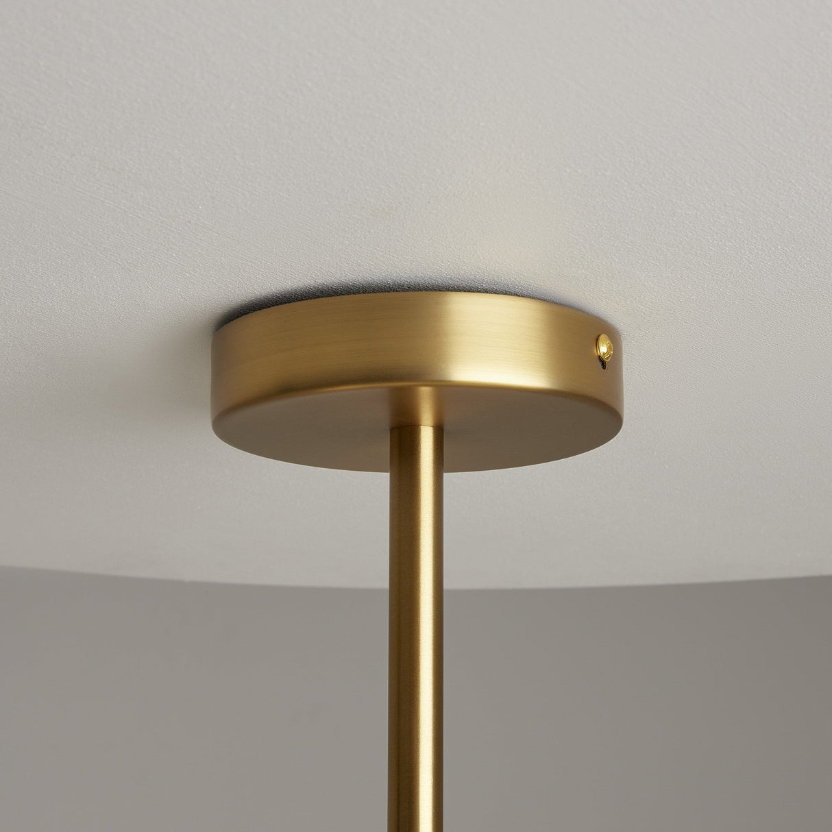 Close-up of the Tropic 6 Light Chandelier - Brass against a white ceiling. This minimalistic and contemporary fixture has a sleek cylindrical metal base with a satin brass finish, extending downward with its rod design.