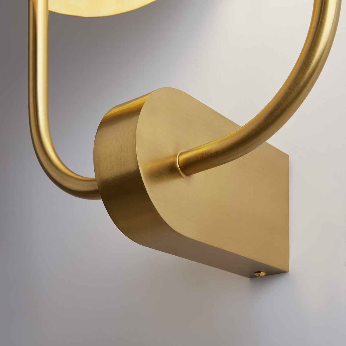 Close-up of the Tropic 2 Light Right High Wall Light in brass, evoking a luxurious tropical getaway with its smooth, curved design against a light grey background. This fixture showcases a sleek and minimalist aesthetic.