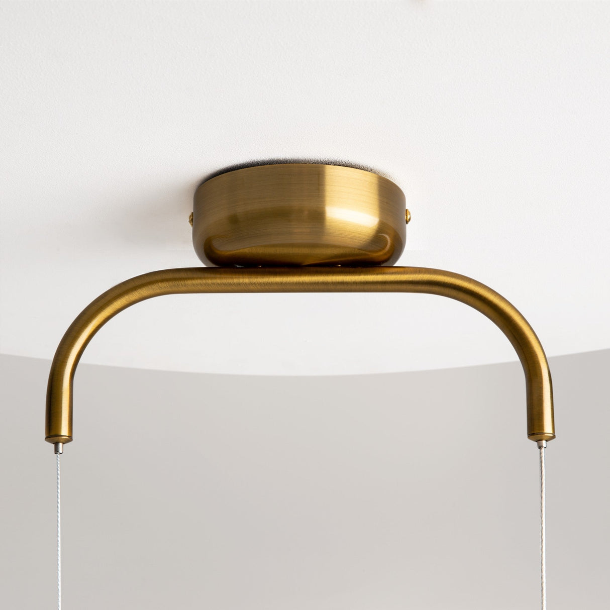 Close-up of the Cabaret LED Pendant Light - Brass, showcasing its modern curved design. The fixture has a smooth semi-circular shape and is ceiling-mounted with two thin wires on a neutral white background.