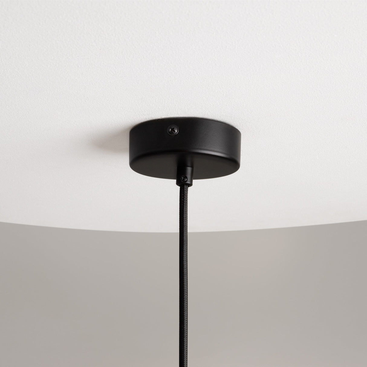 A close-up of the Mood Globe Pendant Light - Black With Clear Glass shows its sleek circular base and clear glass shade, with a black cable elegantly hanging against a white ceiling background.