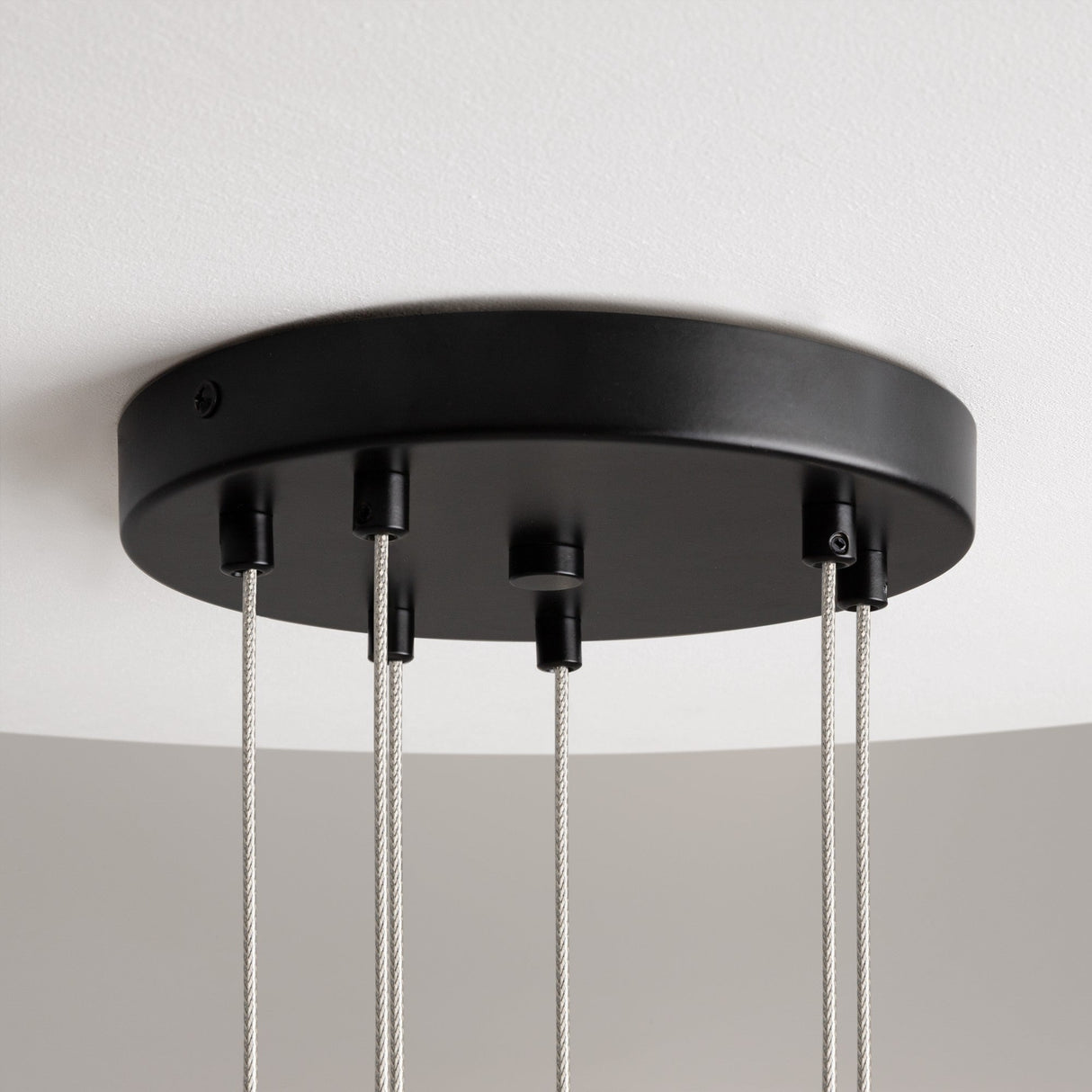The Mood 6 Light Suspension in black, featuring clear glass and five cables, exudes modern elegance while hanging gracefully against a white ceiling.