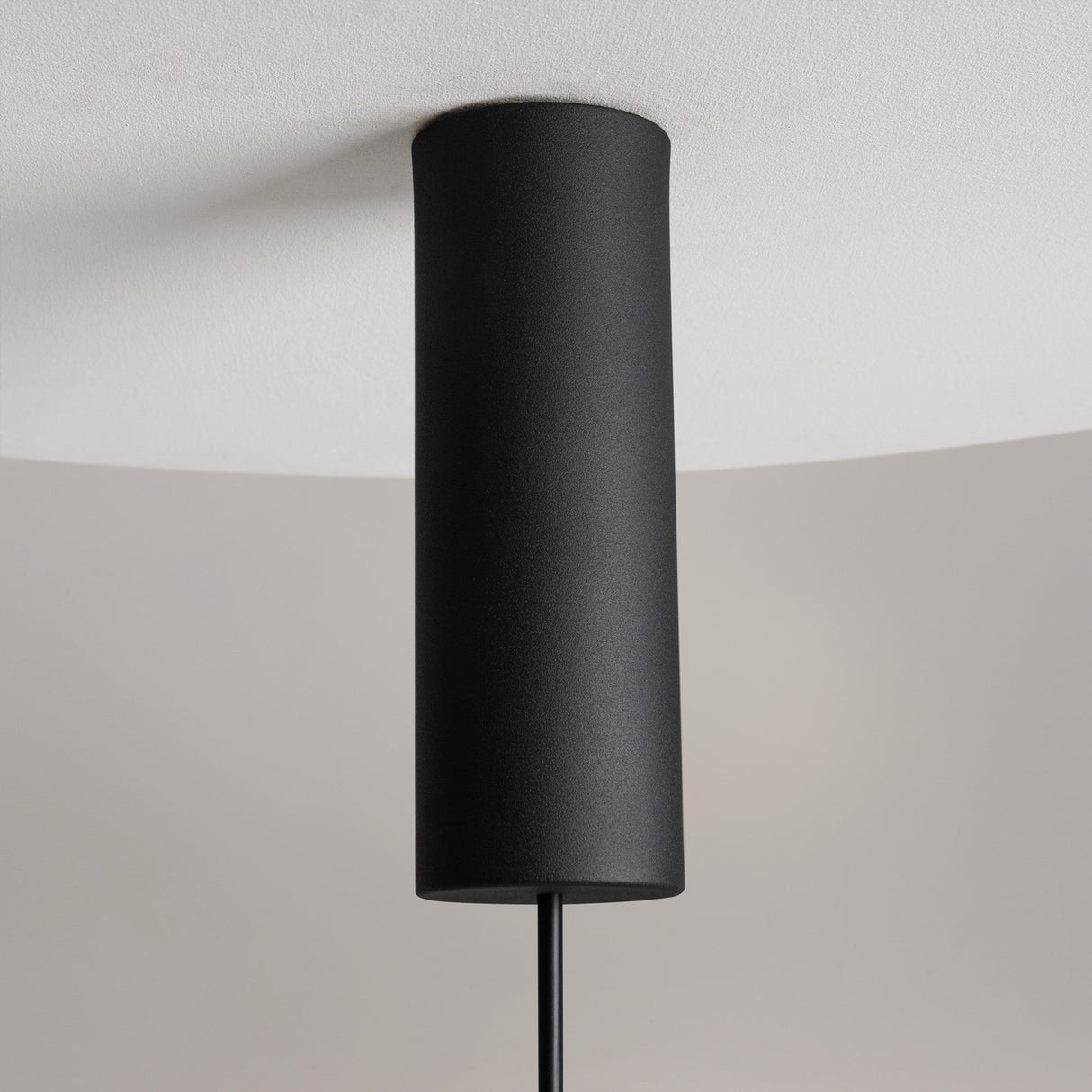 The Nebula LED Pendant Light 20cm is a minimalist cylindrical black fixture with a smoky black glass sphere, beautifully mounted on a white ceiling against a neutral-toned wall, enhancing the simplicity and modern aesthetics of contemporary interiors.