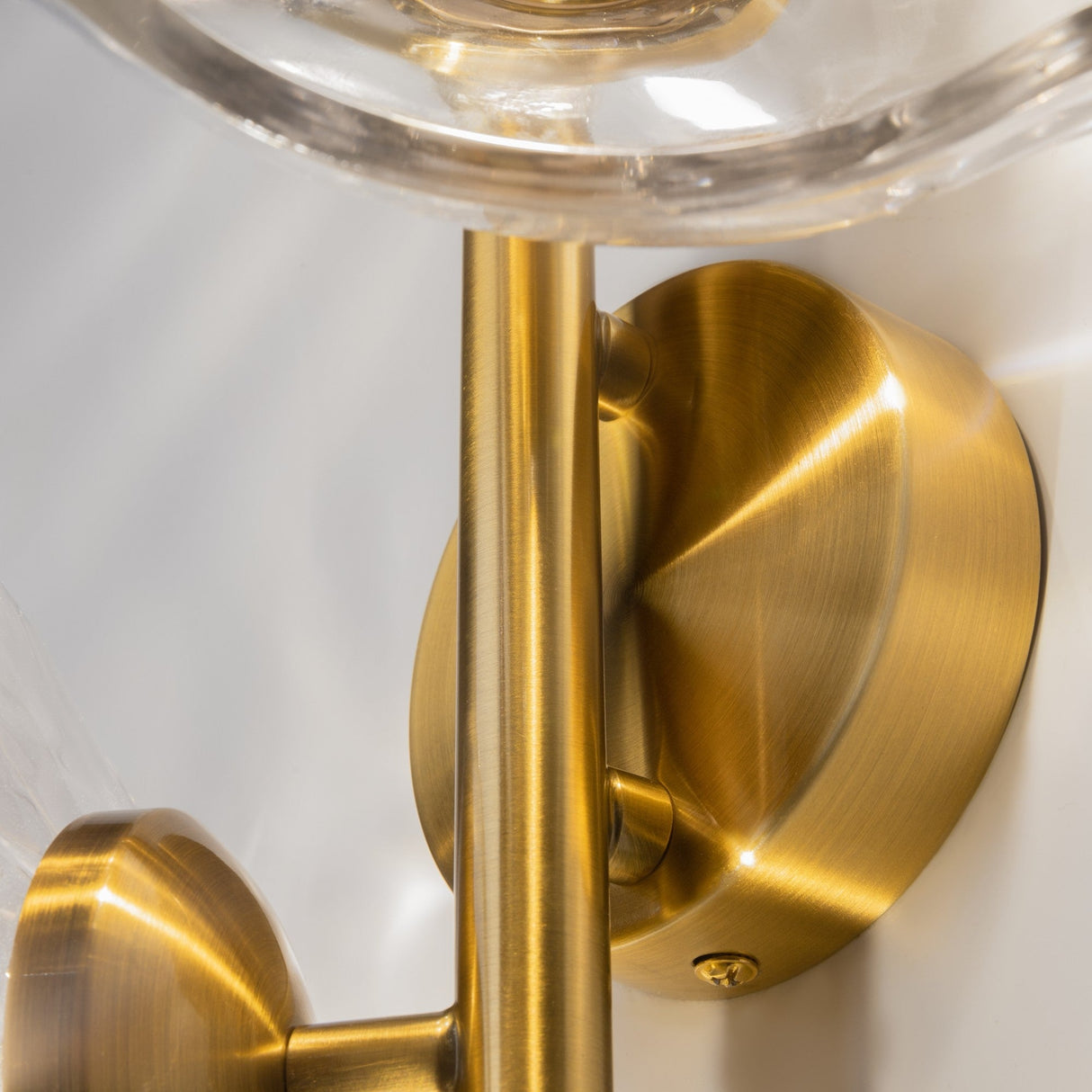 The Miracle 4 Light Wall Light features a brass design with a vertical cylindrical stem, art-inspired elegance from its round base and smooth surfaces. Partially visible cast glass shades contribute to the soft shadows on the wall.