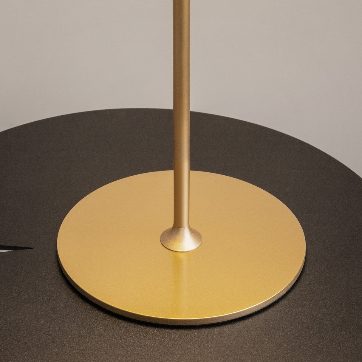 Close-up of the AI Collaboration Rechargeable LED Table Lamp - Gold with its pole centered on a gold base, contrasting against the matte black tabletop.
