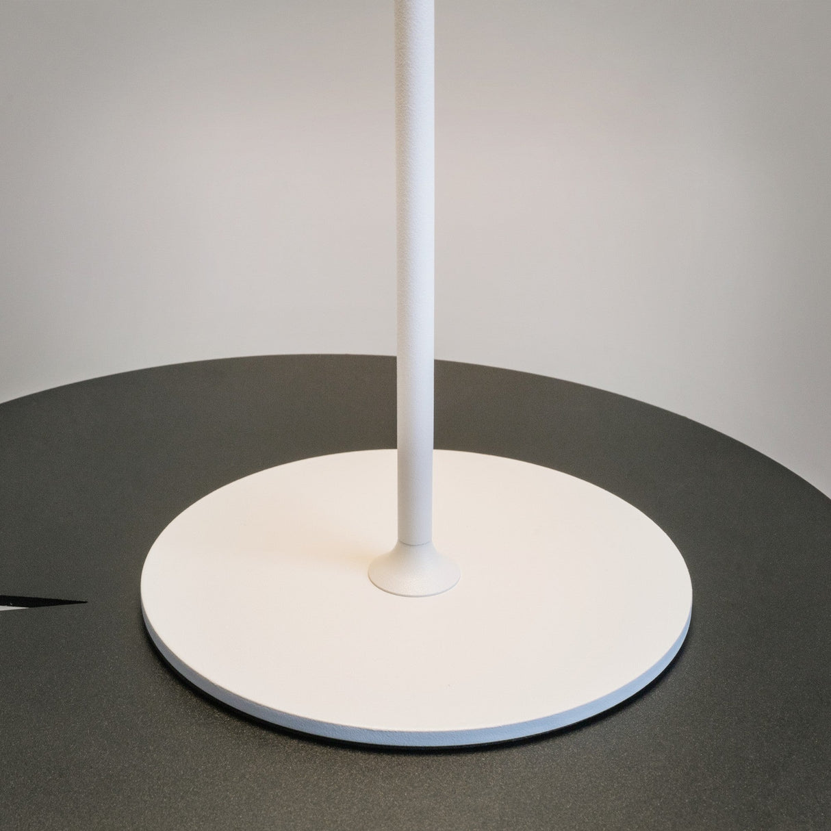 The AI Collaboration Rechargeable LED Table Lamp - White features a round base on a dark table, with its pole extending vertically to emphasize its minimalist design against a light gray backdrop, highlighting this eco-friendly lighting solution.
