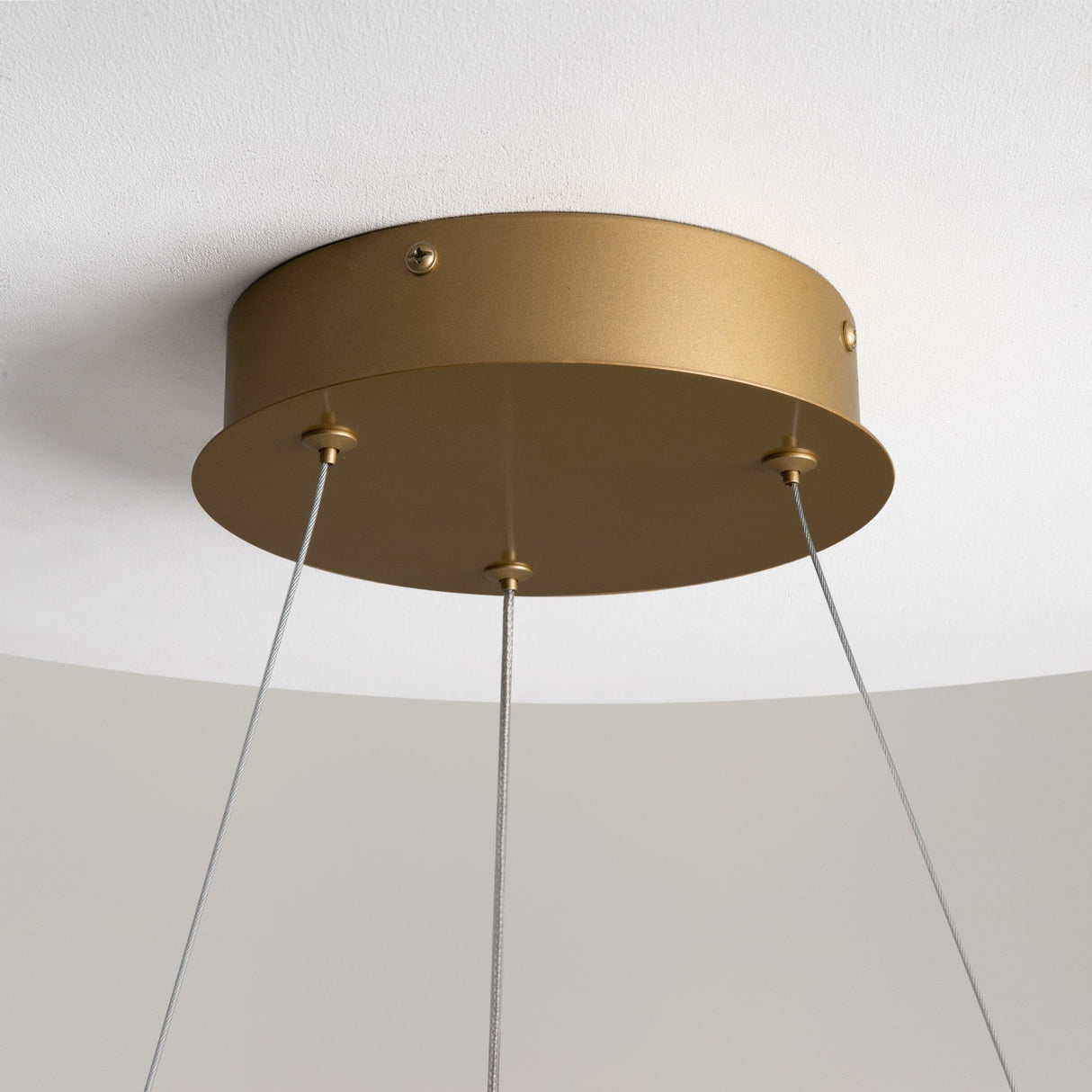The Curve LED Dimmable Spiral Suspension Light - Brass shows a ceiling-mounted gold fixture with three thin wires in a brass finish on a white ceiling. Its adjustable color temperature adds versatile and modern elegance to any space.