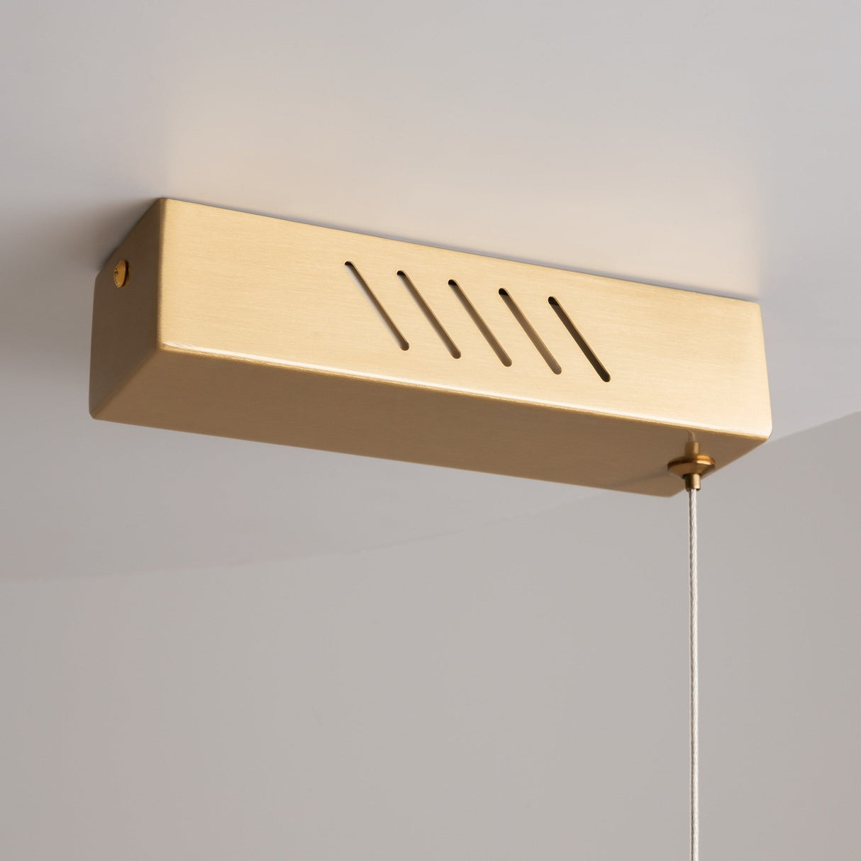 A minimalist brass fixture mounted on the ceiling, the Petra LED Linear Suspension Light features diagonal slits and a thin pull cord. Seamlessly integrating into contemporary interiors, its elegant and simple design makes it a standout piece.