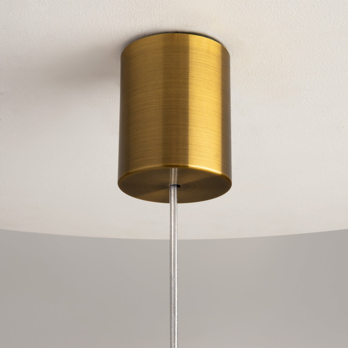 A close-up of the Frozen 1 Light Pendant showcases a cylindrical brass canopy and sleek metal rod with a wood-cut clear cast glass shade. The neutral ceiling highlights its minimalist, nature-inspired design.