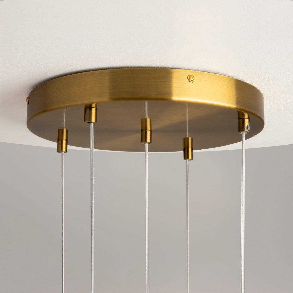 A close-up of the Frozen 5 Light Cluster Pendant - Brass shows its matte brass fixture with cast solid glass lampshades, suspended by four wires against a white ceiling and neutral gray backdrop.