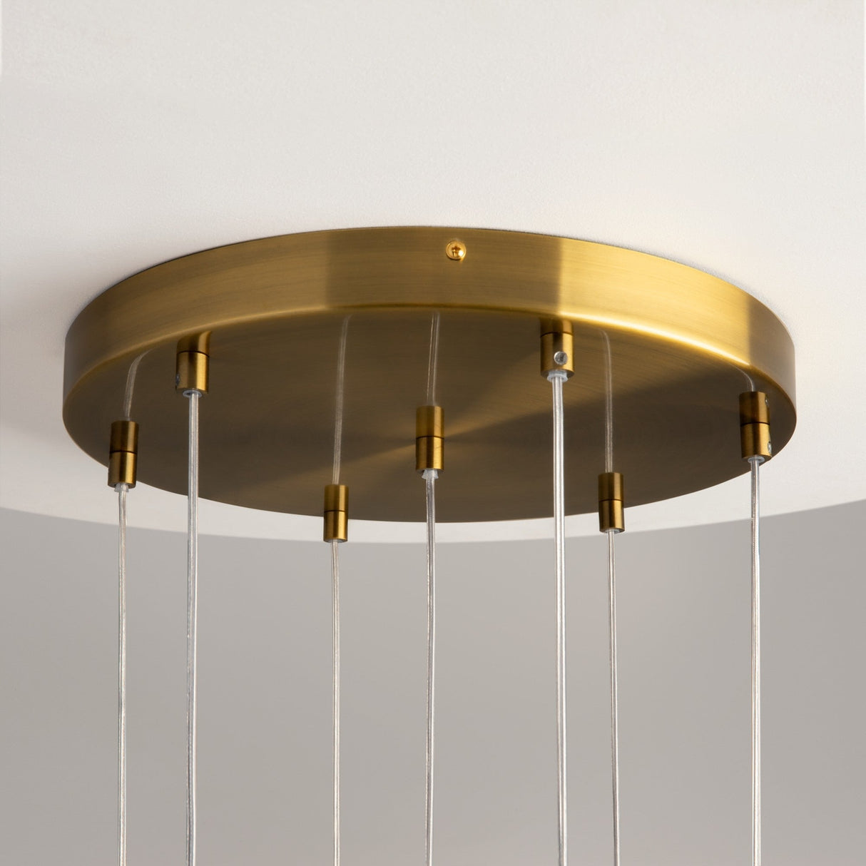 The Frozen 7 Light Cluster Pendant - Brass is a contemporary chandelier with a circular brass base on a white ceiling. Slim cables descend, each holding a cast glass light fixture, while the bulbs are hidden in the photo.