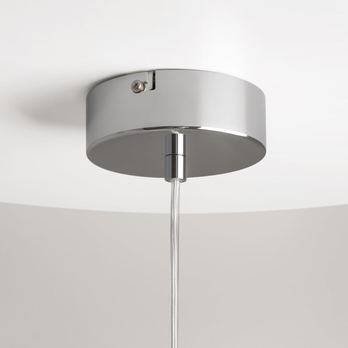 The Drop LED Pendant Light - Chrome features a sleek design with a chrome ceiling fixture and round base mounted on a white ceiling, highlighted by a single thin wire extending downward from the center.