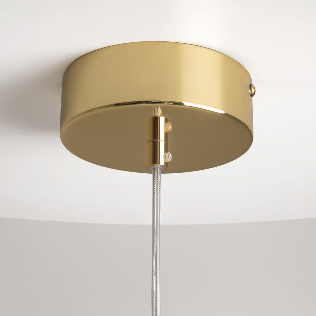 The Drop LED Pendant Light - Gold features a sleek, modern design with a cylindrical base and transparent adjustable cord. It elegantly hangs from a white ceiling, enhancing contemporary décor.