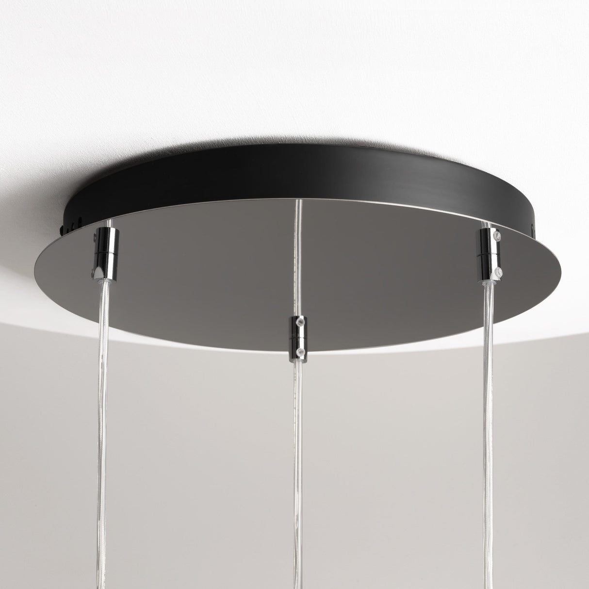 The Drop LED Cluster Pendant Light 33W 3000K - Chrome is a circular black ceiling fixture with three elegantly hanging cables and silver connectors, mounted on a white ceiling. It offers a sleek, modern design perfect for energy-efficient lighting in any room.
